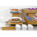 A hotel buffet table with white bowls and a natural bamboo shallow rectangular basket filled with food.