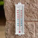 A Taylor utility wall thermometer on a brick wall with red and blue lines showing the temperature.
