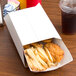 A table with a clay coated kraft food tray sleeve with fried chicken and french fries in it and a plastic cup filled with a brown liquid.