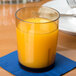 A light amber Cambro plastic tumbler filled with orange juice on a table.