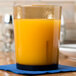 A Cambro light amber plastic tumbler filled with orange juice on a table