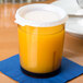 A close-up of a Cambro light amber plastic cup filled with orange liquid on a table with a blue napkin.
