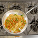 A Vollrath Wear-Ever saute pan filled with noodles and vegetables on a stove.