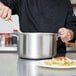 A person stirring pasta in a Vollrath stainless steel sauce pot.