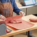 A person in a brown apron in a butcher shop using Choice pink butcher paper to wrap meat on a table.