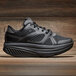 A black Shoes For Crews Energy II athletic shoe on a wood surface.