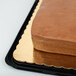 A rectangular brown cake on a gold laminated rectangular cake pad.