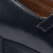 A close up of a black leather shoe with stitching and a buckle on the side.