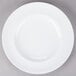 An Arcoroc white porcelain dinner plate with a circular pattern on a gray surface.