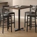 A Lancaster Table & Seating black cast iron bar table base on a table with black chairs.