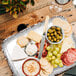 A rectangular melamine platter with cheese, crackers, and grapes on a table with a bowl of green olives.