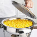 A person holding a Vollrath stainless steel food pan lid over a pan of corn.