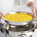 A hand in a plastic glove using a Vollrath stainless steel food pan to serve yellow corn.