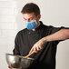A man wearing a light blue Mercer Culinary face mask while cooking.