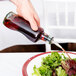 A hand pouring Tablecraft olive oil from a bottle onto a salad plate of green and red salad.