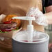 A person putting sauce on a burger using a Carlisle pump.