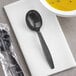 A black plastic spoon on a napkin next to a bowl of soup.