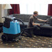A man using a Mytee carpet extractor to clean a couch in a lounge area.