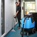 A man using a Mytee Contractor's Special heated carpet extractor to clean a blue carpet in a hallway.