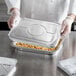 A chef putting a Choice half size aluminum foil steam table pan lid on a tray of food.