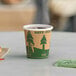 A close-up of a EcoChoice Kraft paper hot cup with a tree print filled with coffee on a table.