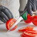 A person in a black glove using a Dexter-Russell scalloped utility knife to slice a tomato.
