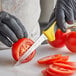 A person in black gloves using a Dexter-Russell scalloped utility knife to cut a tomato.