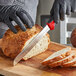 A person in black gloves using a Dexter-Russell scalloped bread knife to cut a loaf of bread.