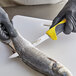 A person in a black glove using a Dexter-Russell narrow boning knife with a yellow handle to cut a fish.