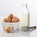 A white container of brown eggs with a whisk and a bottle of milk.