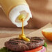 A person using a FIFO Innovations squeeze bottle to put mustard on a hamburger.