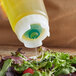 A person using a FIFO thin squeeze bottle to pour oil onto a salad.