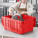 A woman in a chef's uniform putting a metal object in a red plastic Orbis tote box.
