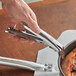 A person using an American Metalcraft nickel-plated steel pizza pan gripper to lift a deep pan of pizza.