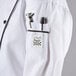 A close up of a Chef Revival ladies white long sleeve coat with black piping and a pocket with a pen in it.