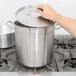 A person holding a Vollrath Optio stainless steel stock pot lid over a large pot on a stove.