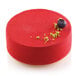 A red round cake with a blueberry on top in a Silikomart silicone baking mold.