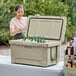 A woman putting green bottles into a CaterGator outdoor cooler on a table.