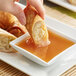 A hand dipping a fried egg roll into a bowl of Lee Kum Kee Gold Label Plum Sauce.