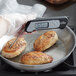 A person using a CDN ProAccurate digital folding thermometer to check food temperature in a frying pan.