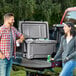 A man and woman standing next to a CaterGator outdoor cooler in the back of a truck with cans inside.