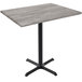A Holland Bar Stool EnduroTop bar height table with a black cross base and a greystone wood laminate top.