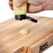 A hand holding a yellow bottle of John Boos Block Board Cream over a cutting board.