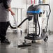 A man using a Lavex stainless steel wet/dry vacuum to clean a kitchen floor.