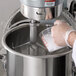 A person pouring liquid into a metal container using an Avantco commercial mixer.