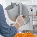A person using an Avantco stand mixer with a shredder attachment to cut carrots.