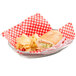 A Tablecraft large oval stainless steel basket with a sandwich and chips inside on a white table.