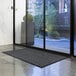 A charcoal Lavex Water Absorbent parquet entrance mat in front of a glass door.