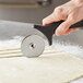 A person using an Ateco stainless steel pastry cutter with a black handle to cut dough.