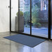 A blue Lavex Needle Rib indoor entrance mat roll on the floor in front of a glass door.